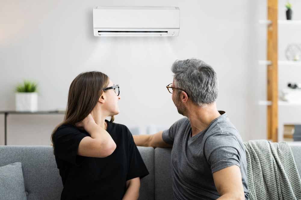 Couple looks at air coming out of air conditioning unit.