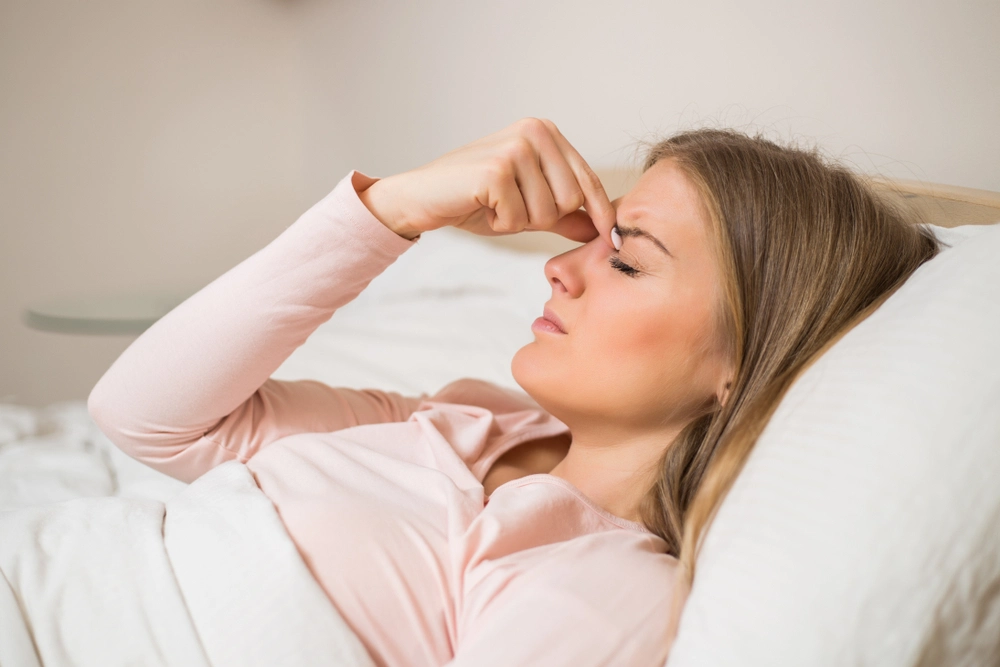Sick looking woman pinches her brow while laying down.