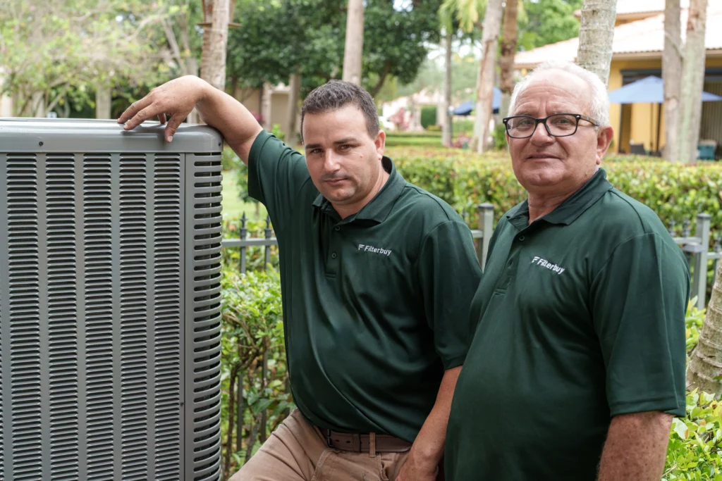 An image of two professional HVAC technicians from Filterbuy standing beside a residential outdoor AC unit, representing reliable local HVAC installation services.